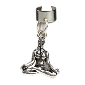 May include: Silver-toned ear cuff with a dangling charm depicting a seated yoga figure in a meditative pose. The charm is detailed with the figure's features and clothing. The ear cuff is designed to clip onto the ear.