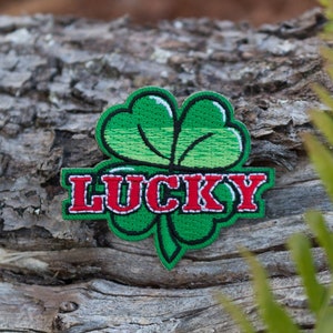 May include: Green embroidered patch with a four-leaf clover and the word "LUCKY" in red lettering.