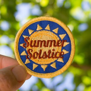 May include: A yellow and blue embroidered patch with a sun design and the text "Summer Solstice".
