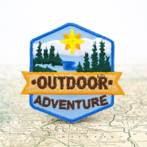 embroidered iron on patch with the words outdoor adventure across it with a nature scene of trees, a river and a sun on it