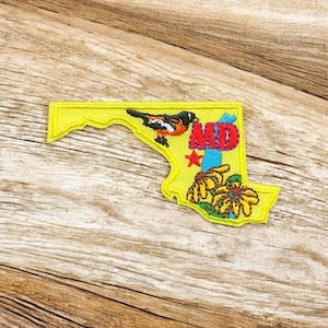 May include: Embroidered patch in the shape of Maryland, featuring a colorful bird, flowers, and the letters "MD." The patch is yellow with red, orange, blue, and green details. The patch is likely for a jacket or bag.