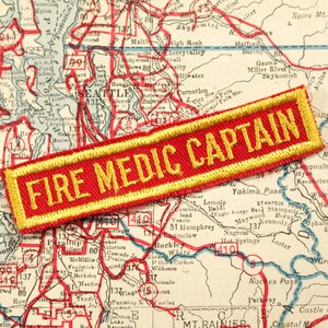May include: A red and gold embroidered patch with the text "FIRE MEDIC CAPTAIN" on a vintage map of Washington state.
