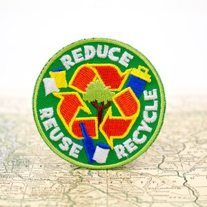 May include: A green, circular patch with the words "Reduce, Reuse, Recycle" in white lettering around a red, orange, and yellow recycling symbol. A small green tree is in the center of the symbol.