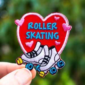 May include: Embroidered patch featuring a red heart with the words "ROLLER SKATING" in turquoise. Below the heart are white roller skates with black and yellow accents. Pink hearts are embroidered around the heart.