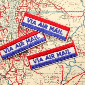 May include: Three red, white, and blue fabric patches with the text "VIA AIR MAIL" on a vintage map.