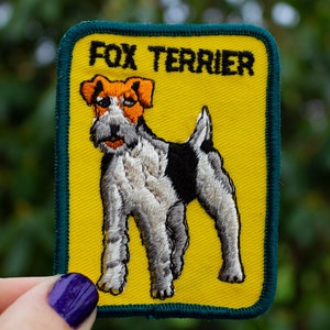 May include: Embroidered patch featuring a Fox Terrier dog. The patch has a yellow background with a green border. The dog is depicted in black, white, and brown, with the words "FOX TERRIER" in black letters at the top.