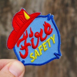 May include: A blue and red embroidered patch with a firefighter's hat and the words "Fire Safety" in yellow thread.