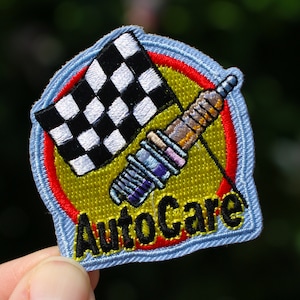May include: A blue and yellow embroidered patch with a checkered flag and a spark plug. The text "AutoCare" is embroidered in black on the patch.