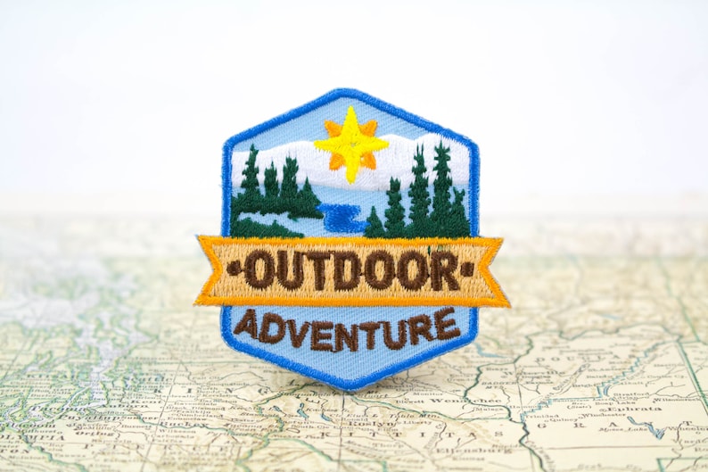 embroidered iron on patch with the words outdoor adventure across it with a nature scene of trees, a river and a sun on it