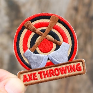 May include: A brown and red embroidered patch with a target and two crossed axes. The text "AXE THROWING" is on a brown banner below the target.