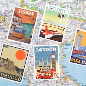 May include: Five vintage travel postcards featuring illustrations of Lisbon, Portugal; Toulon, France; London, England; Morocco; and Pisa, Italy. The postcards are arranged on a map of Europe.