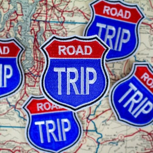 May include: Five blue and red road trip patches with white text that reads "ROAD TRIP". The patches are on a vintage map background.