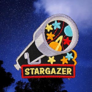 May include: A black and white embroidered patch with a telescope pointed at a starry night sky. The telescope is filled with colorful stars, planets, and a rocket. The text "STARGAZER" is written in yellow on a red banner.