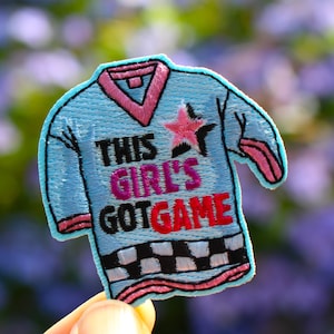 May include: A blue and pink embroidered iron-on patch with a star and the text "This Girl's Got Game".