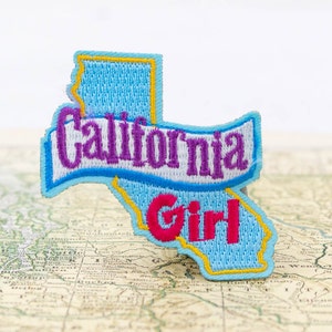 May include: A blue and yellow embroidered patch shaped like the state of California with the text "California Girl" in purple and pink lettering.