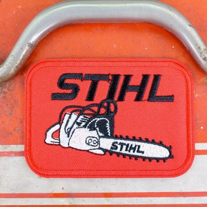 May include: Red embroidered patch with a white chainsaw and black text that reads "STIHL" above the chainsaw and "STIHL" on the chainsaw.