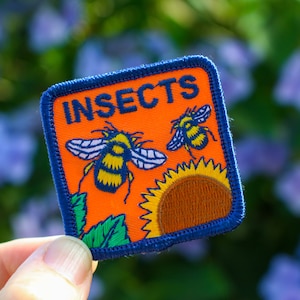 May include: A blue and orange embroidered patch with the word "INSECTS" in white text. The patch features two cartoon bees on a sunflower.