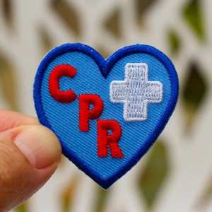 May include: A blue heart-shaped patch with the letters CPR in red and a white cross on the right side.