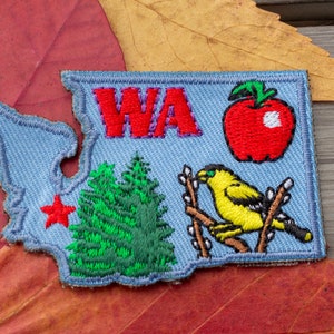 May include: A blue felt patch in the shape of the state of Washington with the letters "WA" in red, a red apple, a green evergreen tree, and a yellow bird on a branch.