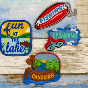 May include: Four embroidered patches with a summer lake theme. The patches are blue, red, green, and yellow. The patches feature the words "Fun at the Lake", "Fishing", "Swimming", and "Canoeing".
