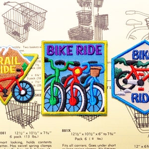 May include: Three embroidered iron-on patches featuring a mountain scene with a red bicycle, a blue scene with three bicycles, and a blue scene with a red bicycle. The patches are labeled "Trail Ride", "Bike Ride", and "Bike Ride".