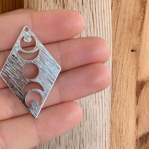 May include: Silver-toned metal charm in the shape of a diamond with a cut-out design of three crescent moons.