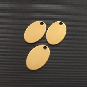 May include: Three gold oval-shaped metal tags with a hole at the top. The tags are on a black textured surface.