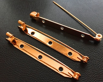 May include: Three gold-toned metal safety pin backs. The pins are different lengths and have multiple holes along the back.