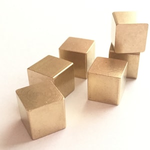 May include: Five small, gold-colored metal cubes stacked on top of each other. The cubes are smooth and have a slightly shiny finish.