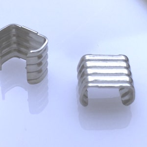 Puede incluir: Dos terminales de cordón de metal plateado con un diseño acanalado. Los terminales de cordón están diseñados para ser utilizados con un cordón o una cuerda.