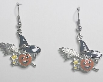 Pode incluir: Um par de brincos de Halloween prateados com uma abóbora esculpida com um chapéu de bruxa e uma vassoura.