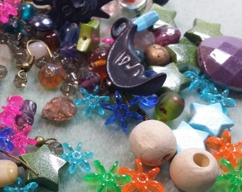 May include: A collection of colorful beads and charms, including stars, flowers, and a sun and moon charm. The beads are made of various materials, including wood, plastic, and metal. The charms are a mix of colors, including blue, green, orange, and purple.