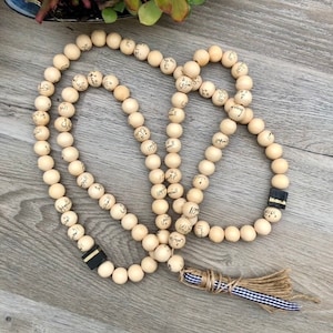 Puede incluir: Un collar de cuentas de oraci&oacute;n de madera con un borla. Las cuentas est&aacute;n inscritas con escritura &aacute;rabe.
