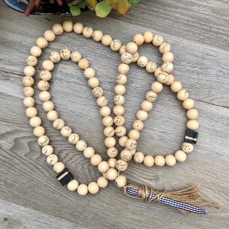 Puede incluir: Un collar de cuentas de oraci&oacute;n de madera con un borla. Las cuentas est&aacute;n inscritas con escritura &aacute;rabe.