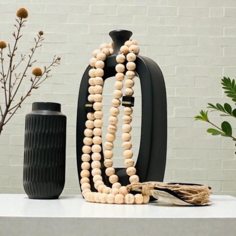 May include: A black, modern-style vase and a tall, black decorative object with a large opening are displayed. A strand of light-colored wooden beads is draped over the black object. A smaller, textured black vase is also present.