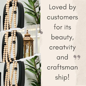 May include: Black metal decorative wall art with a beaded garland. A gold lantern and green plant are visible in the background. Text reads "Loved by customers for its beauty, creativity and craftsmanship!"