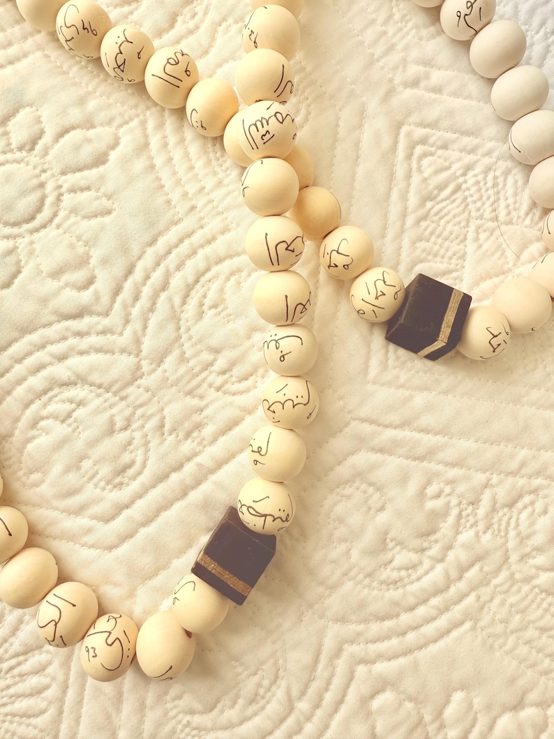 Puede incluir: Un collar de cuentas de oraci&oacute;n blancas con cuentas de madera marr&oacute;n y escritura &aacute;rabe. Las cuentas est&aacute;n enhebradas con un cord&oacute;n delgado. El collar est&aacute; sobre una superficie de tela blanca.