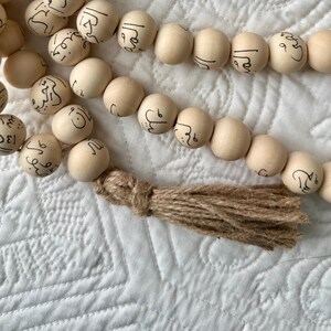 Puede incluir: Una hebra de cuentas de madera con escritura &aacute;rabe en cada cuenta. Las cuentas est&aacute;n enhebradas con una borla marr&oacute;n.