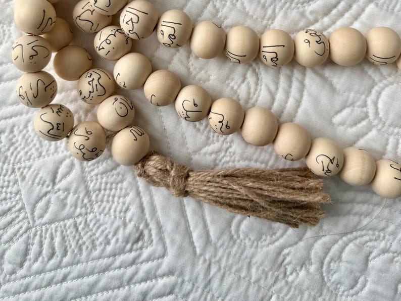 Puede incluir: Una hebra de cuentas de madera con escritura &aacute;rabe en cada cuenta. Las cuentas est&aacute;n enhebradas con una borla marr&oacute;n.