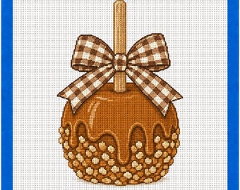 May include: A needlepoint canvas featuring a caramel apple with a wooden stick, topped with a brown and white gingham bow. The apple is coated in smooth caramel with a textured layer of small, light brown nut pieces at the base, all on a white grid.