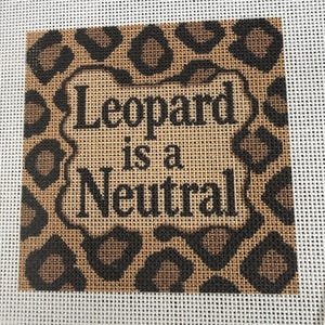 May include: A square needlepoint canvas featuring a brown and black leopard print pattern. Centered on the canvas is a rectangular border containing the black text "Leopard is a Neutral" written in a bold, serif font against a tan background.