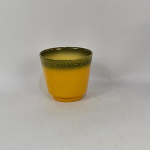 Op de afbeelding: Een gele keramische pot met een groene gespikkelde rand.