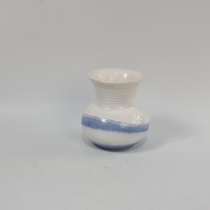 Op de afbeelding: Een kleine witte keramische vaas met een blauwe band rond het midden.