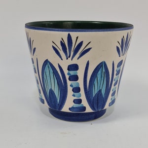Op de afbeelding: Een witte keramische kom met een blauw en groen bloemenmotief. De kom heeft een groene rand en een blauwe basis.