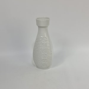 Puede incluir: Un jarrón de cerámica blanco con un diseño texturizado que presenta líneas en relieve y motivos florales.