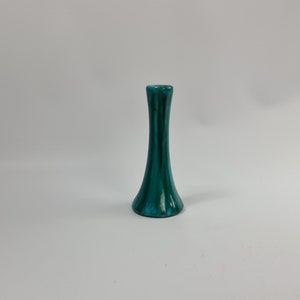 Op de afbeelding: Een kleine, teal-kleurige keramische vaas met een uitlopende basis en een smalle hals.