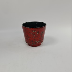 May include: A small red ceramic planter with a black rim and a speckled pattern.