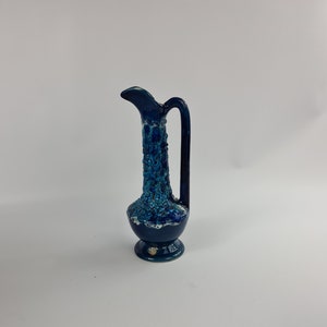 May include: A small blue ceramic pitcher with a textured surface and a handle. The pitcher has a wide base and a narrow neck.