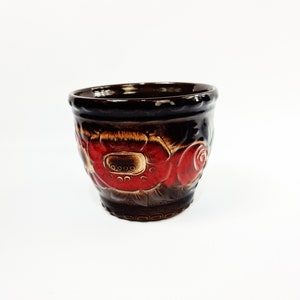 Puede incluir: Una maceta de cerámica marrón con diseños florales rojos y marrones.