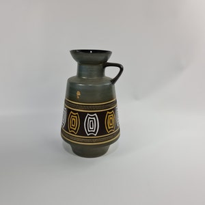 Pode incluir: Um vaso de cerâmica cinza com um padrão geométrico marrom, branco e amarelo. O vaso tem uma boca larga e uma alça.
